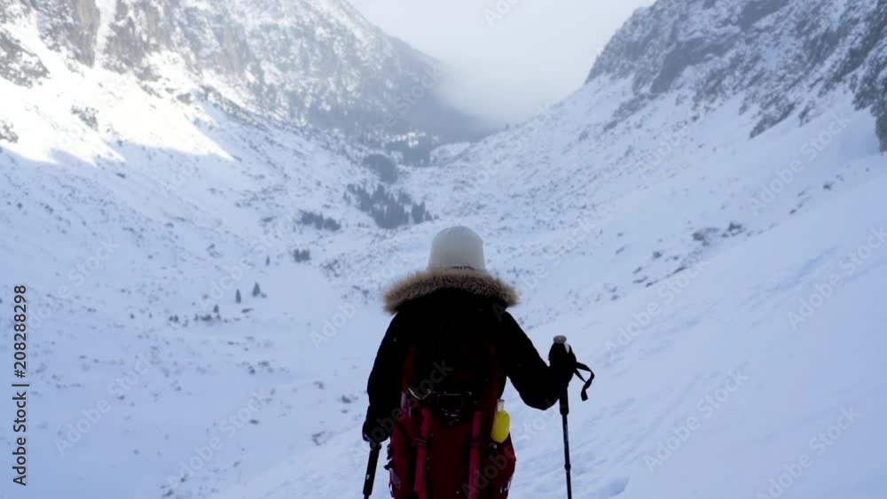 Slow motion of young woman hiking in rocky mountains landscape covered in snow during cold weather Slow motion of young woman hiking in rocky mountains landscape covered in snow during cold weather