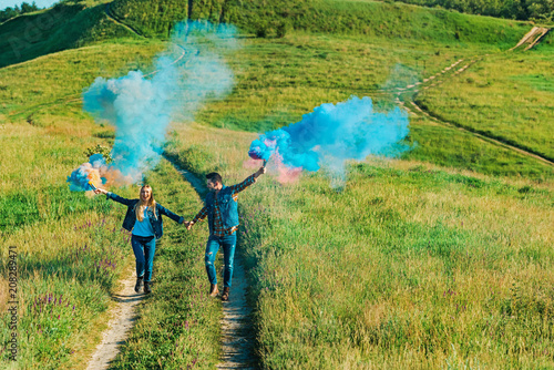 elevated view of couple holding colorful smoke bombs on rural meadow