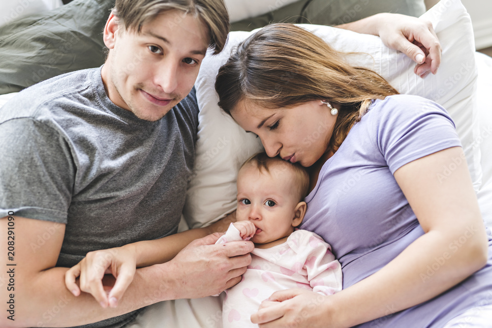 Portrait of beautiful young parents and cute baby on bed