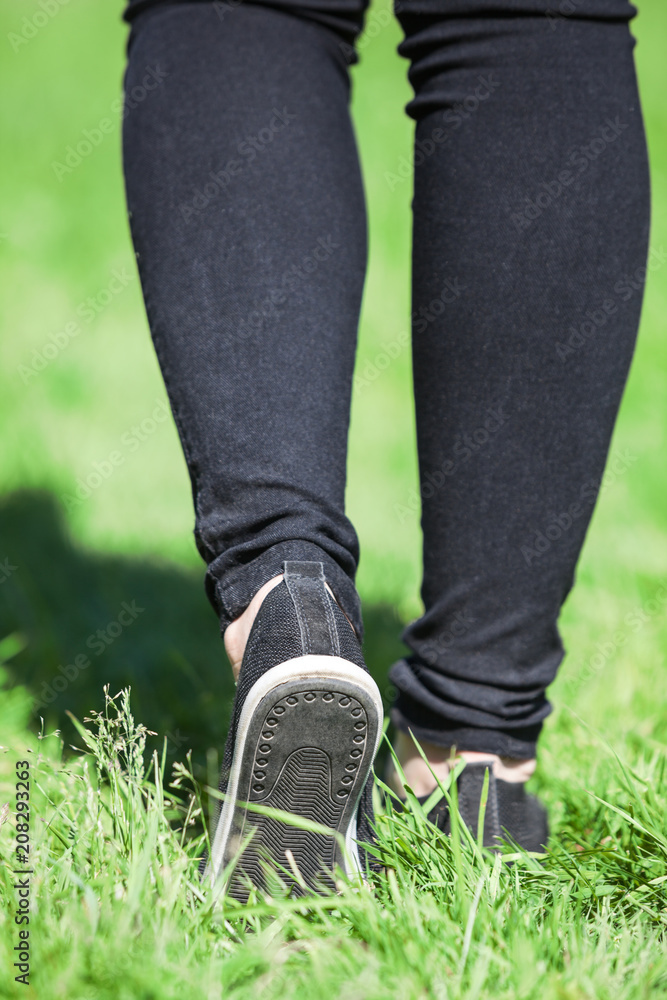 Female legs walking on green grass, rear view, black jeans and light moccasins Female legs walking on green grass, rear view, black jeans and light moccasins