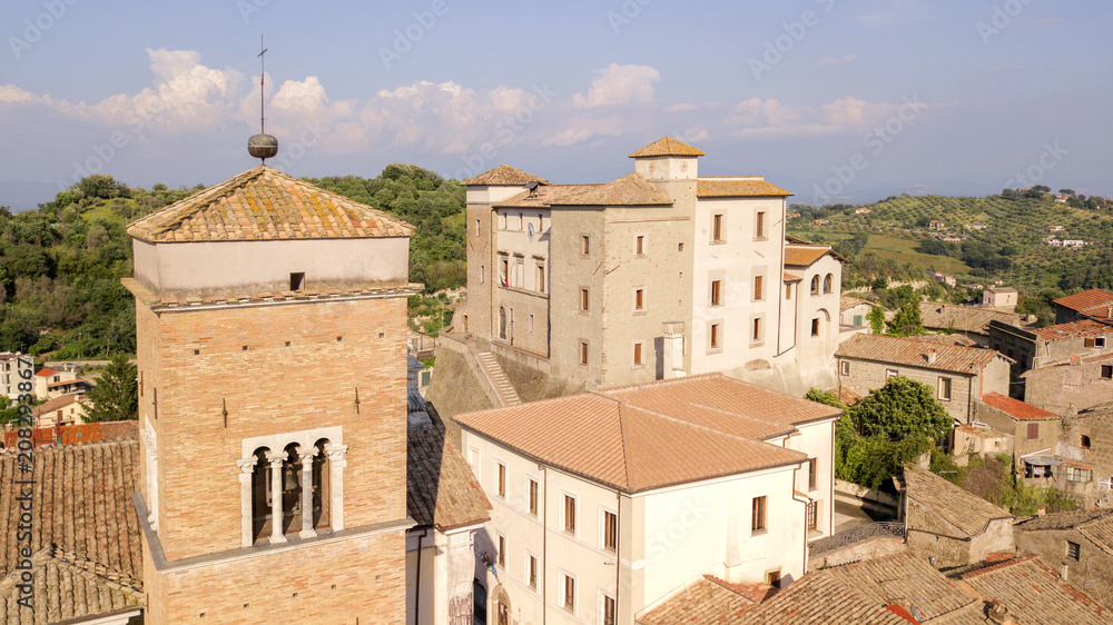 Aerial view of Castelnuovo di Porto castle, near Rome in Italy. The building has a square shape with four towers at the corners. In the foreground the cross of the church bell tower.