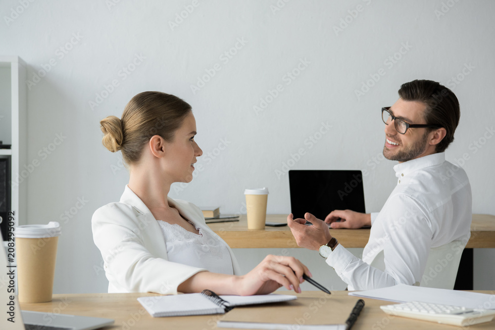 happy young business colleagues chatting at workplace in office happy young business colleagues chatting at workplace in office