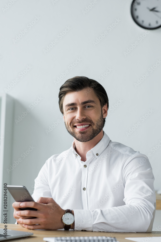 happy young businessman using smartphone at workplace and looking at camera happy young businessman using smartphone at workplace and looking at camera