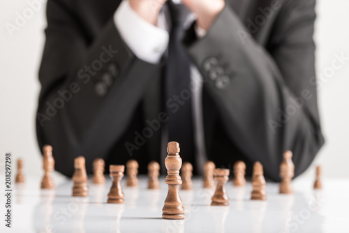 Businessman in business suit planning strategy with dark chess figures