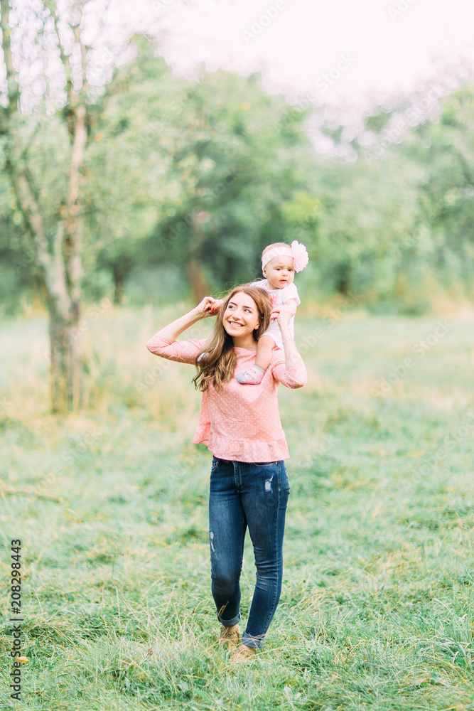 Obraz premium Mother and little daughter playing together in a park. Happy cheerful family. Mother and baby kissing, laughing and hugging in nature outdoors