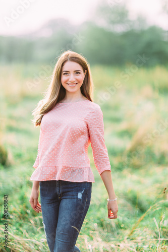 Fototapeta Naklejka Na Ścianę i Meble -  Beauty young girl outdoors enjoying nature. Fashion young woman in pink shirt and jeans in meadow