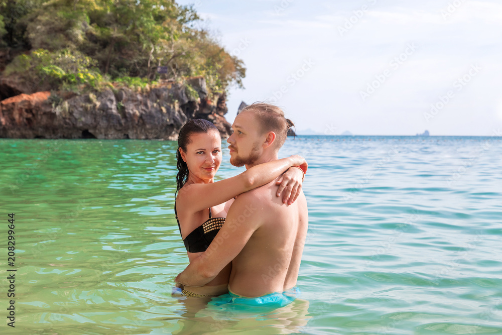Young slim happy hipster couple on tropical beach kiss each other