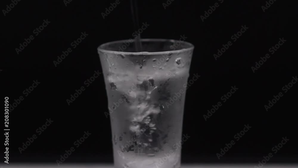 Pour alcohol into the glass. A glass of vodka on the table. The sweating glass of vodka. Slow motion is poured into a glass of vodka. Pour alcohol into the glass. A glass of vodka on the table. The sweating glass of vodka. Slow motion is poured into a glass of vodka.