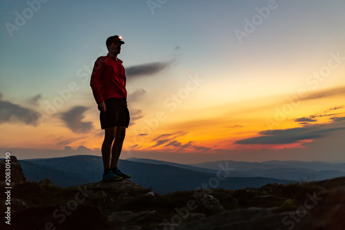 Trail runner with head lamp on top of mountain peak at night.