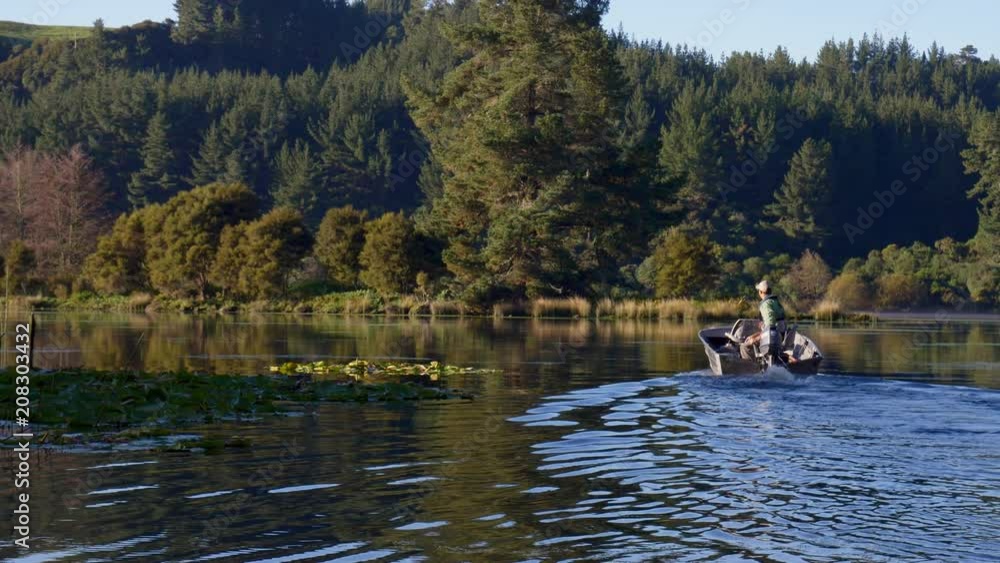 Fly fisherman in boat driving on scenic Lake Whakamaru in New Zealand to go fishing Fly fisherman in boat driving on scenic Lake Whakamaru in New Zealand to go fishing