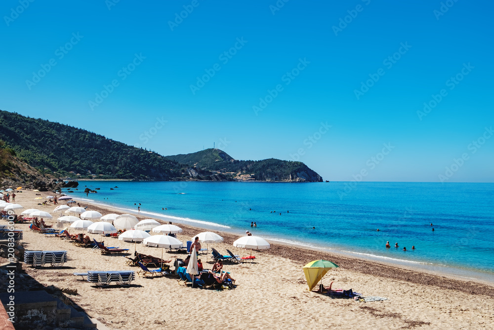 View of the Pefkoulia Beach, Lefkada island, Greece. Tourists, sunbeds and umbrellas on idyllic sunny day.