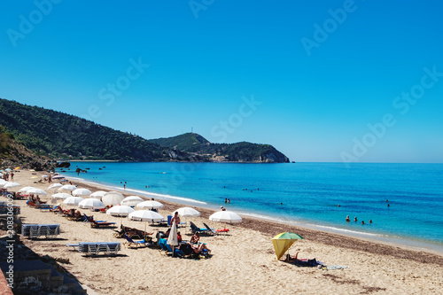 View of the Pefkoulia Beach, Lefkada island, Greece. Tourists, sunbeds and umbrellas on idyllic sunny day.
