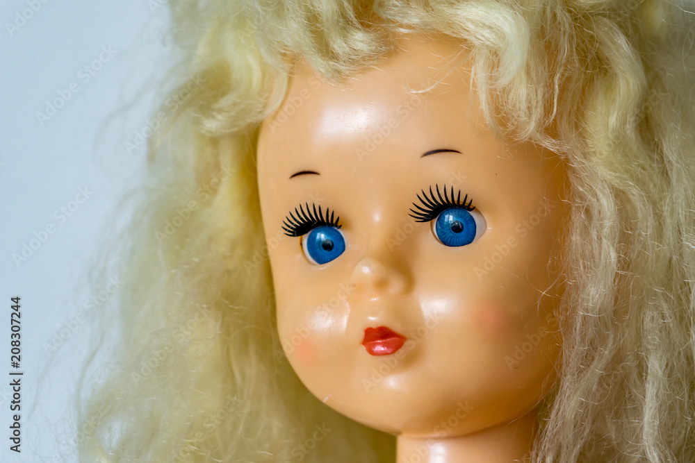 Close-up of beautiful plastic doll with blond hair and blue eyes, sky blue vintage dress and leather shoes. Little princess games.
