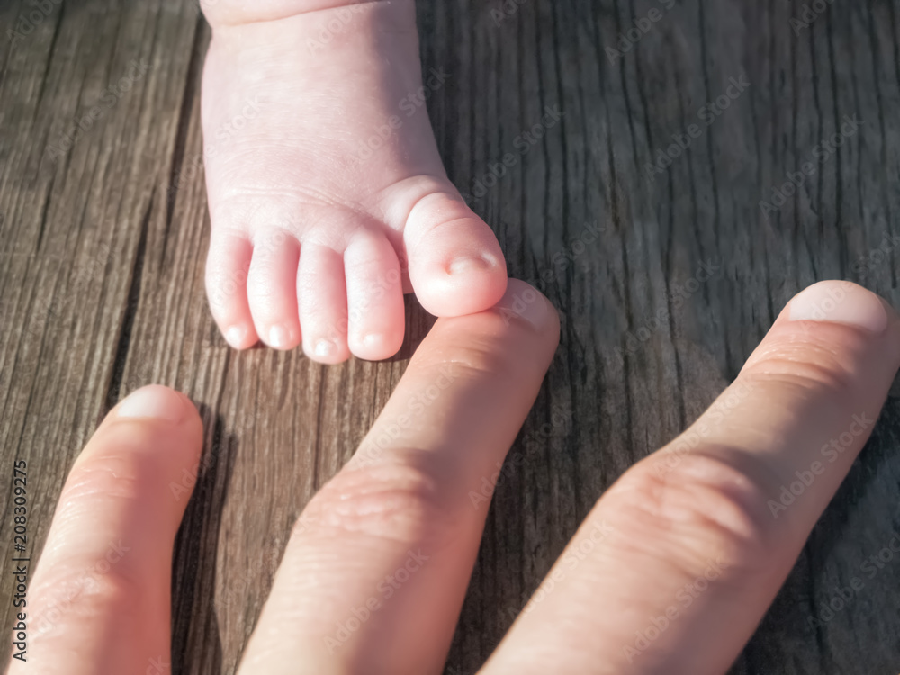 Toddler's foot stepping on mother's finger, rustic wooden background Toddler's foot stepping on mother's finger, rustic wooden background