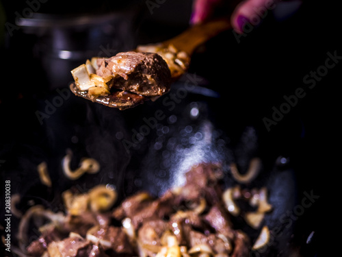 close up woman holding fried meat with vegetables above frying pan with dark background © Mihail