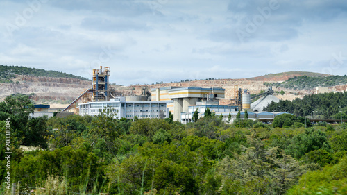A huge and working cement production plant production factory on mining quarry. Heavy indusrty with a lot of machinery. Chemical production and harm to environment