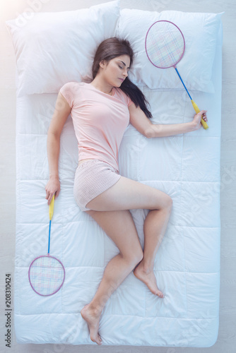 Sporty dreams. Top view on a sporty woman holding badminton rackets while lying in bed and sleeping tight at home.