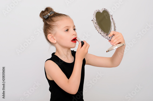 Pretty small female child making visage with glass mirror.