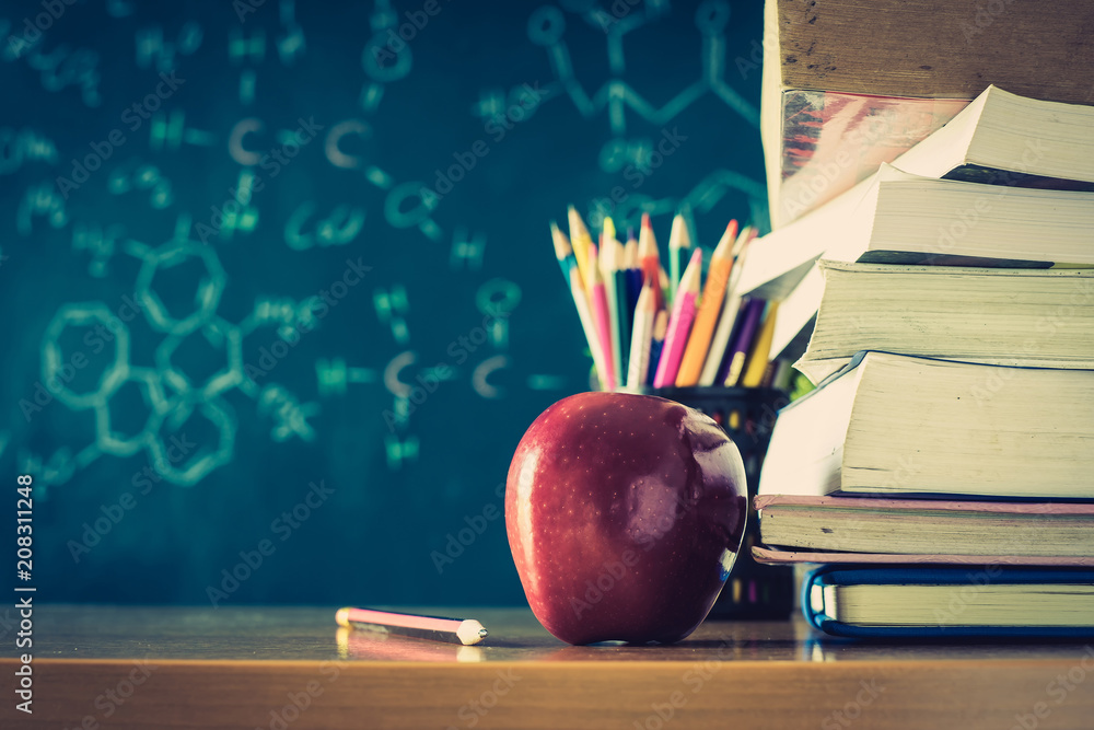 School books with red apple on desk over green school board background