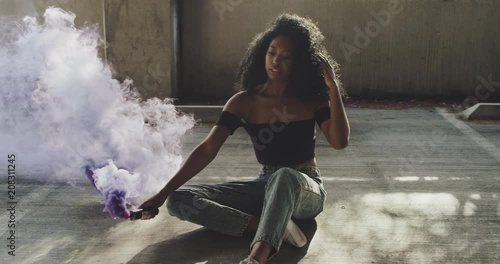 Beautiful young woman modeling with purple smoke grenade in dramatic moody lighting 