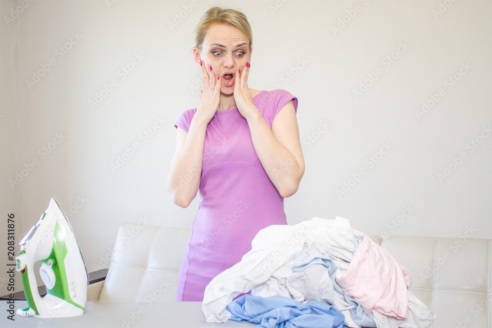 Not happy housewife portrait with iron and many cloth on backgro Not happy housewife portrait with iron and many cloth on backgro