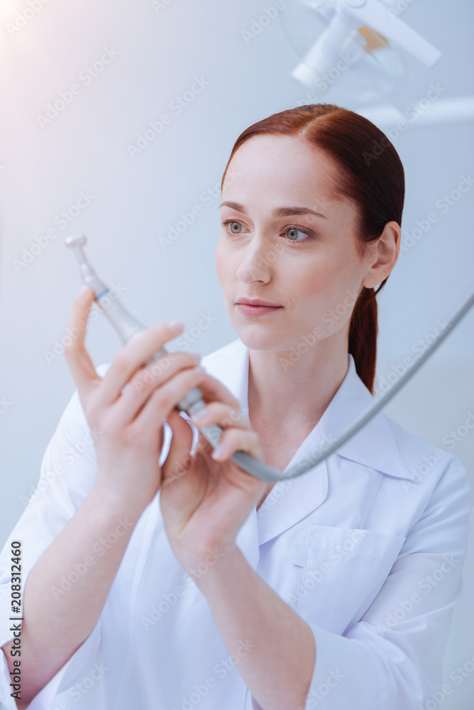 Sterile instrument. Delighted female person keeping smile on her face and holding special tool while looking at it Sterile instrument. Delighted female person keeping smile on her face and holding special tool while looking at it