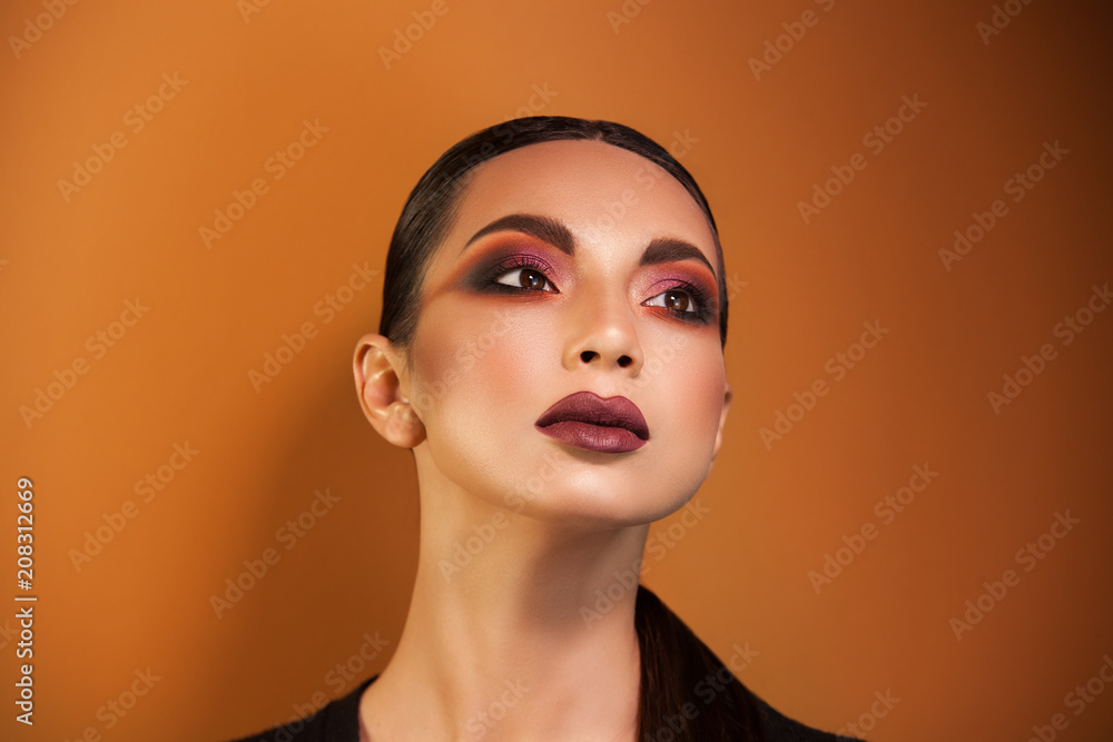 slightly throws back our head, we see a thin, delicate neck, whose gaze is directed into the distance, an unusual makeup accentuates her eyes, lipstick orange image background. slightly throws back our head, we see a thin, delicate neck, whose gaze is directed into the distance, an unusual makeup accentuates her eyes, lipstick orange image background.