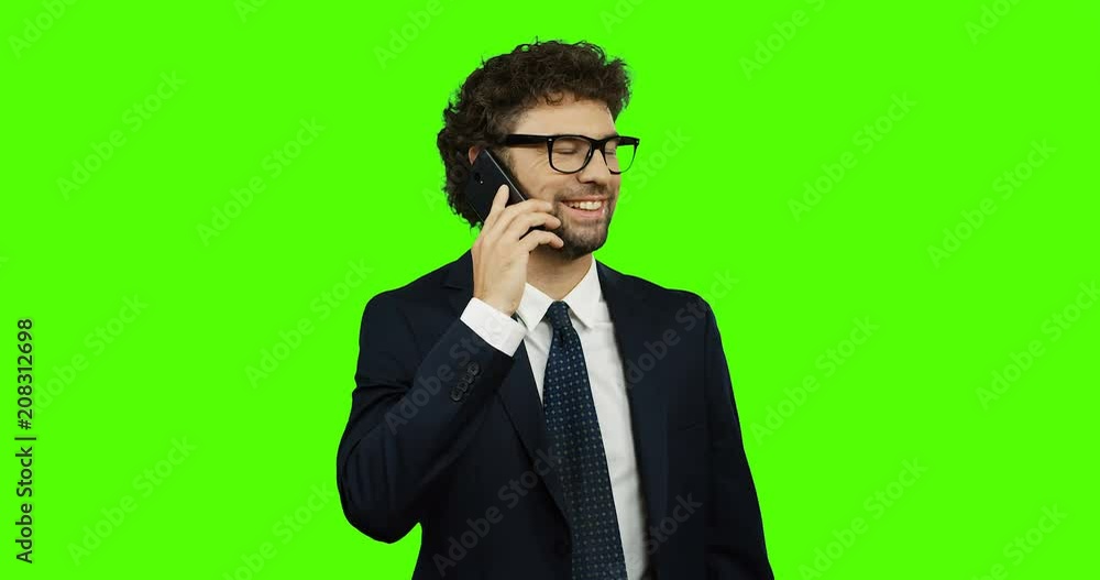 Attractive Caucasian man in the glasses, suit and tie talking on the phone cheerfully on the chroma key background. Green screen.
