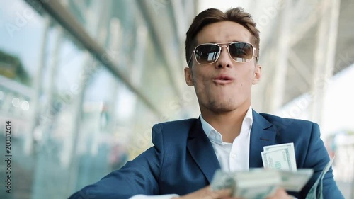 Young happy businessman scatter the dollars in the street. It is located near the office center, slow motion. Successful business or winning the lottery