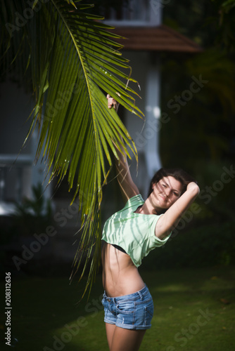 Portrait of a beautiful girl with palm leaf shadows on her face against the cottage background