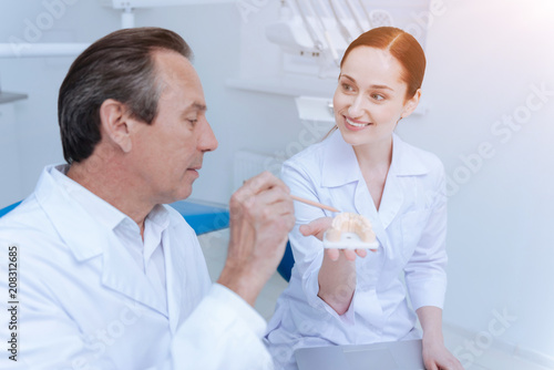 Be serious. Competent dentist keeping pencil in right hand while using it for showing teeth