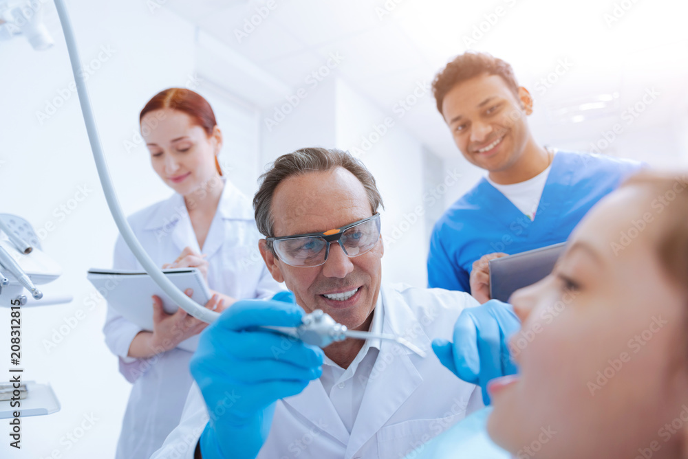 Fototapeta premium I will treat you. Responsible female making notes while observing the process of treatment and standing behind her mentor