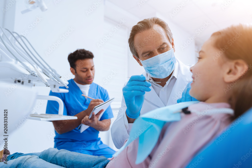 Sterile work. Competent dentist having mask on face and bowing head while doing teeth checkup Sterile work. Competent dentist having mask on face and bowing head while doing teeth checkup
