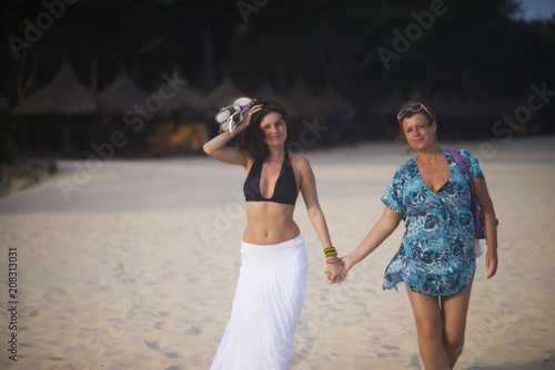 two women holding hands walking on the beach photo