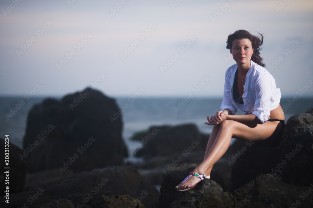 Young beautiful woman sitting on stones in the evening against the sea