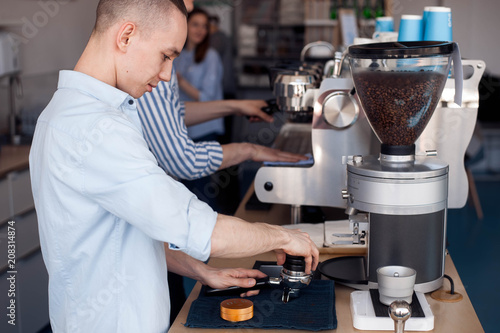 A young guy works as a Barista  he stands at the coffee machine and fills the filter with ground coffee.