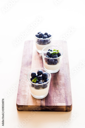 Vanilla pannacotta inside small cup and fresh blueberries. frontal view with golden spoon, and other tools