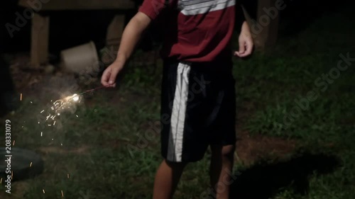 Young 8 year old boy holding a fireworks sparkler away from his body at night