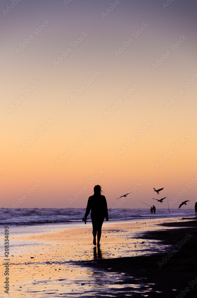 Woman walking on the beach on the sunset