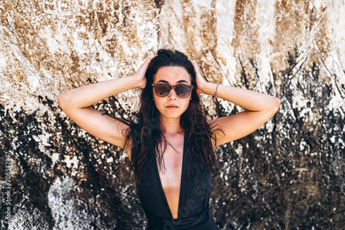 фотографія girl in black swimsuit posing near rock on the beach