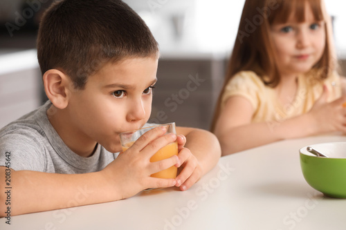 Funny little children drinking citrus juice at home