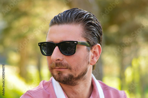 Young man's outdoors portrait looking at the camera who has sunglasses with natural green background. Neutral, happy, sad, disgust, fear, surprise Facial Emotion.