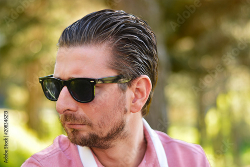 Young man's outdoors portrait looking at the camera who has sunglasses with natural green background. Neutral, happy, sad, disgust, fear, surprise Facial Emotion.