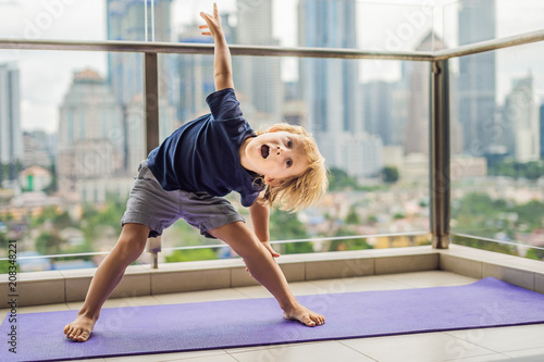 Photos Happy little boy is practicing yoga on his balcony with a panoramic view of the