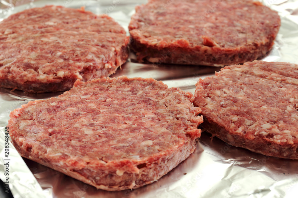 Raw beef burgers on a foil covered baking tray ready to be cooked Raw beef burgers on a foil covered baking tray ready to be cooked
