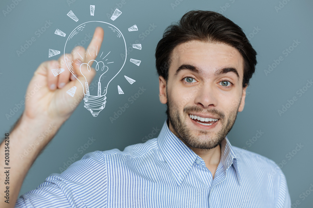 Unexpected idea. Positive creative web developer pointing his finger up while having a wonderful idea