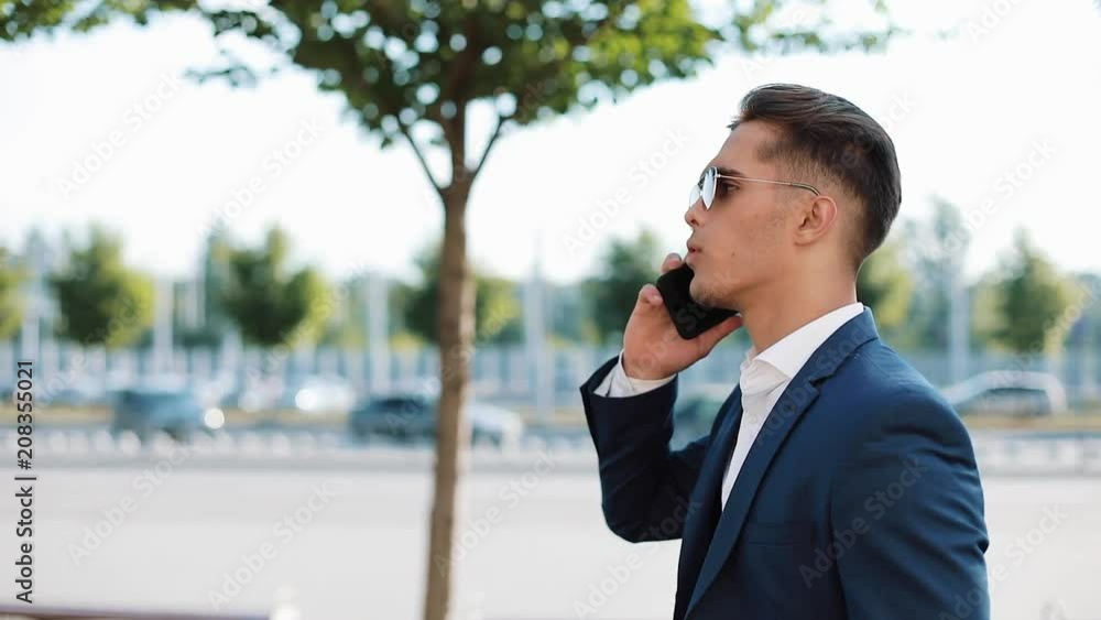 Young businesman in sunglasses talking on his phone and walking in the street. Successful life. Business style, traveler, communication, modern lifestyle. Active lifestyle Young businesman in sunglasses talking on his phone and walking in the street. Successful life. Business style, traveler, communication, modern lifestyle. Active lifestyle