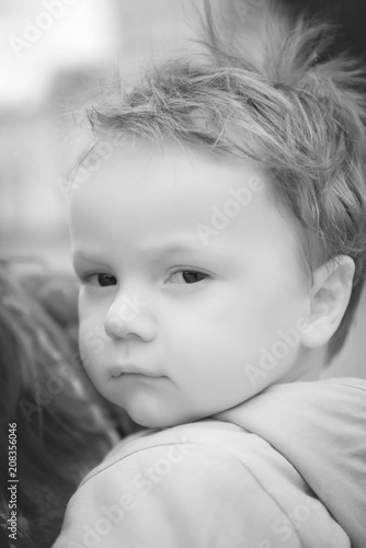 Portrait of a child boy in the arms of a mother with a serious face close-up. Black and white portrait of a child.