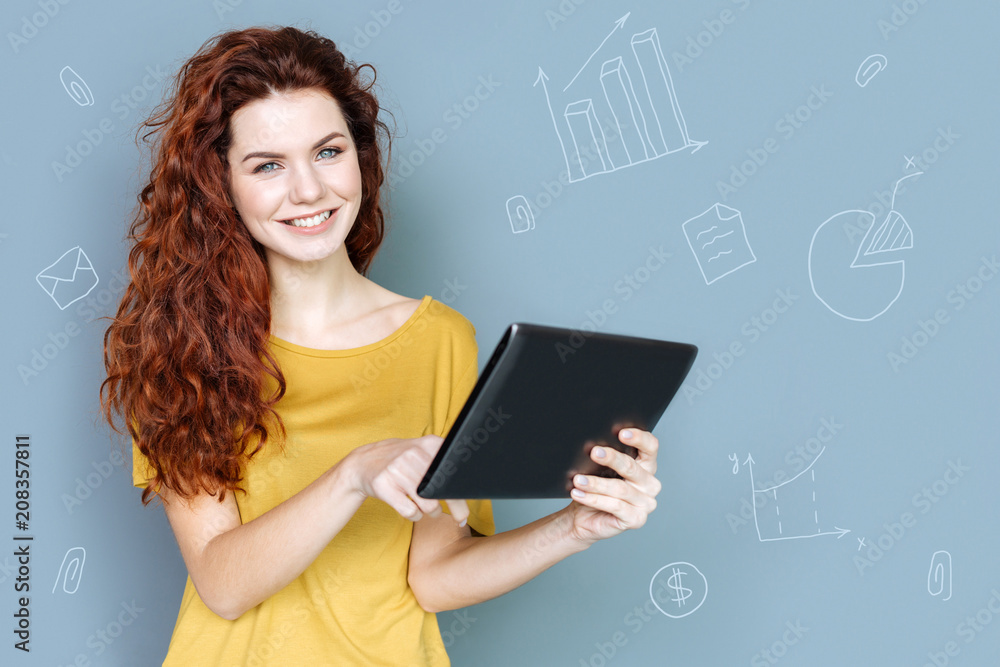 Modern tablet. Positive young economist feeling happy and smiling while standing with a modern tablet in her hands Modern tablet. Positive young economist feeling happy and smiling while standing with a modern tablet in her hands