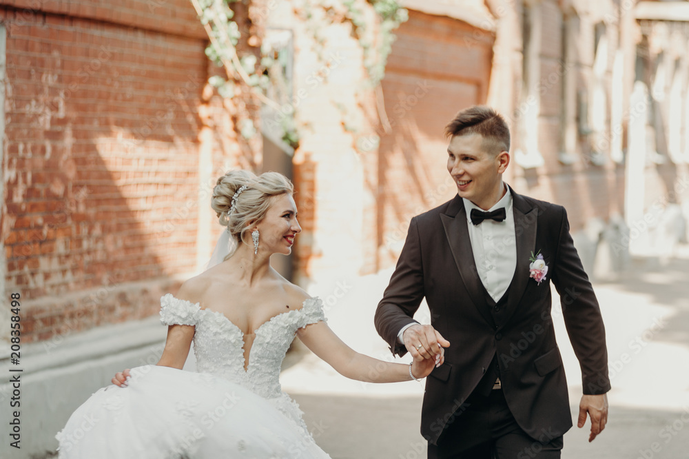 Lovely wedding couple, bride and groom hold each other hands walking in city. Romantic moment on their wedding day.